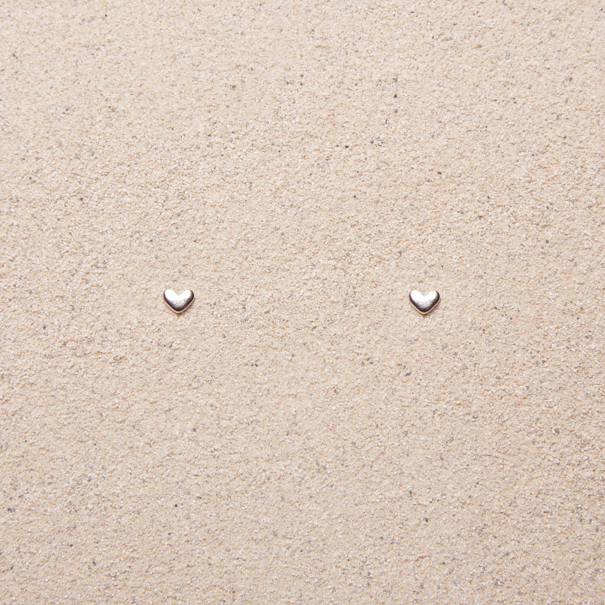 tiny silver heart earrings on a tan background