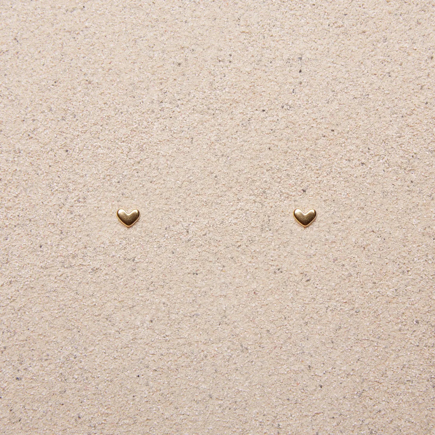 tiny gold heart earrings on a tan background