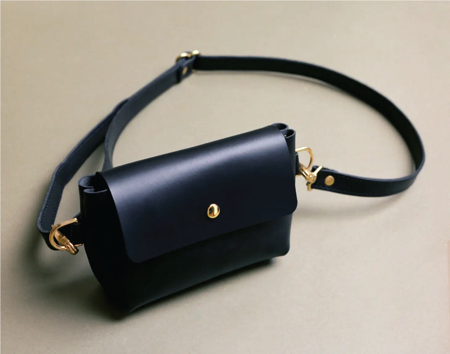 Black leather cross body bag, closed, on flat surface.